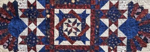 A quilt with a geometric star pattern in red, white, and blue fabrics, featuring American flag and fireworks designs, arranged in a symmetrical, intricate layout—perfect for display at a quilt show in Farmington NM.