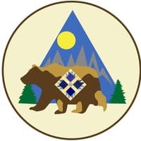 Hudson-River-Piecemakers Logo A circular emblem featuring a brown bear with a blue and white quilt pattern on its side, standing in front of pine trees, mountains, and a yellow sun against a light background.