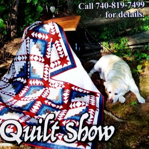 Pieceable-Quilters-Show A red, white, and blue patchwork quilt draped over a chair outside, with a white dog lying nearby on a stone path. Text reads: Quilt Show. Call 740-819-7499 for details.