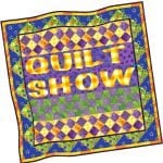 Quilt Show A colorful quilt with patterned borders features the words QUILT SHOW IN IRON MOUNTAIN MICHIGAN in bold yellow letters across the center. The quilt showcases geometric shapes and bright colors like purple, green, orange, and yellow.