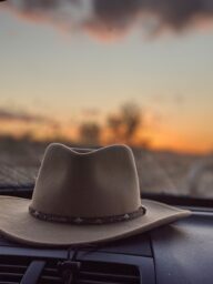 Photo by Ashleigh Stagg Creative hat for men inside of automobile near windshield overlooking colorful cloudy sky at sundown in twilight