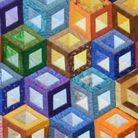 Colorful quilt with a geometric pattern of interlocking cubes in various shades of blue, green, yellow, orange, and purple, creating a striking three-dimensional effect—perfect for display at the Quilt Show in Curtiss, Wisconsin.