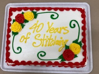 Twin Cities Quilters Guild Rectangular cake with red and yellow rose decorations and a red icing border, crafted to celebrate the Quilt Show in North Tonawanda New York. The cake reads “40 Years of Stitching” in yellow icing, with green vine designs elegantly framing the text.