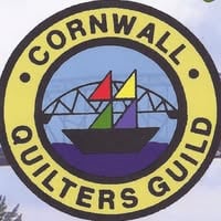 A circular logo with Cornwall Quilters Guild around the edge, featuring a sailboat with colorful sails and a bridge in the background, perfectly captures the spirit of the Quilt Show in Cornwall Ontario.